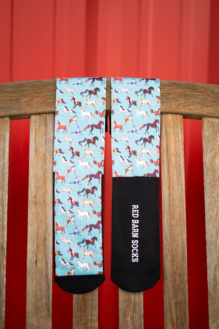 Light blue petite-height socks with colorful horse pattern and black toe and heel displayed on a wooden surface