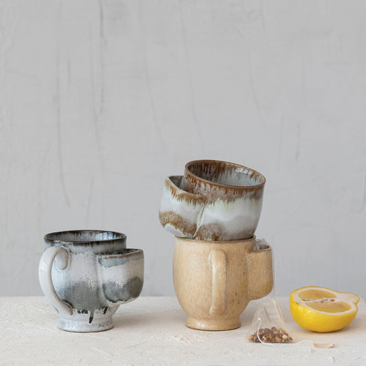 Three ceramic mugs of different sizes on a light surface with a neutral background