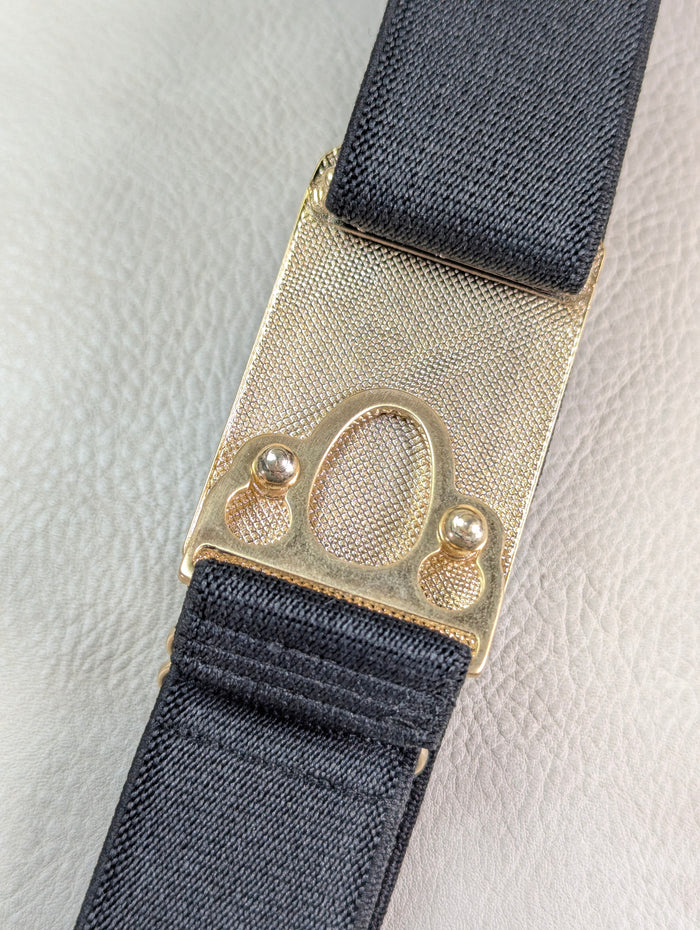 back side of the huston ellany signature gold buckle with black elastic on a beige leather background