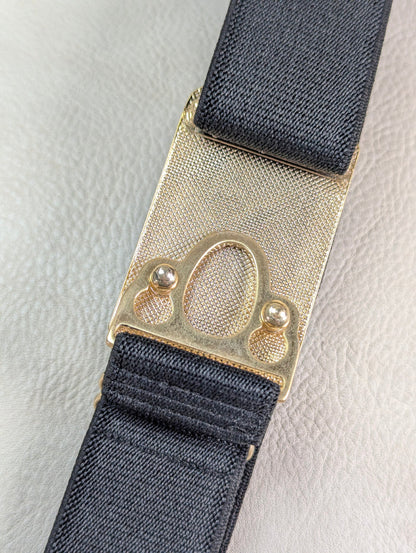 back side of the huston ellany signature gold buckle with black elastic on a beige leather background