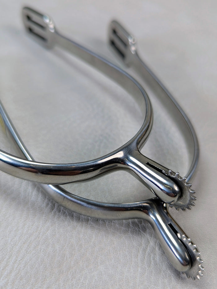 closeup of silver english riding spurs with small rowels on a textured background