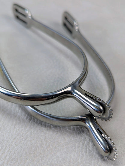 closeup of silver english riding spurs with small rowels on a textured background