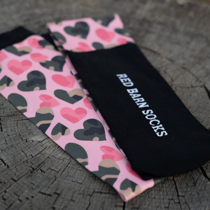 Close‑up of Red Barn Socks showing black logo design and pink Barn Crush heart pattern on wood surface