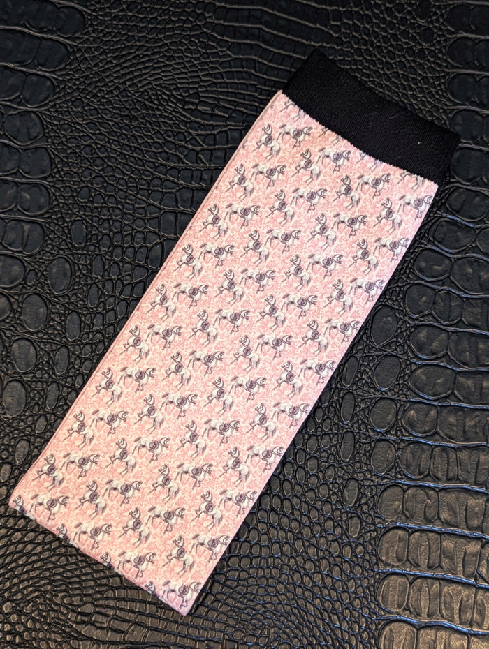 Pink horse‑pattern sock with black cuff displayed on a textured black surface