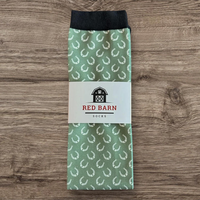 Sage green tall socks with white horseshoe pattern and Red Barn Socks label, folded on a wooden surface