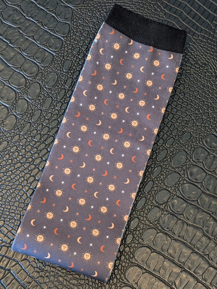Navy sock with celestial sun, moon, and star pattern and black cuff displayed on a textured black surface