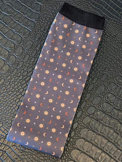 Navy sock with celestial sun, moon, and star pattern and black cuff displayed on a textured black surface