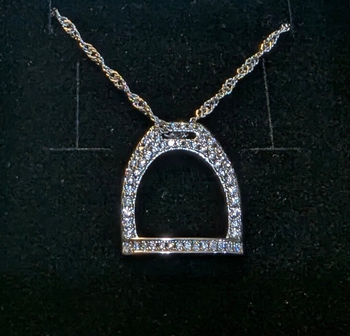 Close‑up of a rhodium plated English stirrup pendant with pavé CZ stones on a twisted sterling silver chain, displayed against a dark textured background.