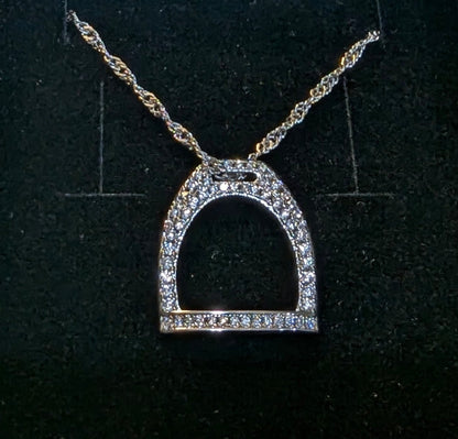 Close‑up of a rhodium plated English stirrup pendant with pavé CZ stones on a twisted sterling silver chain, displayed against a dark textured background.