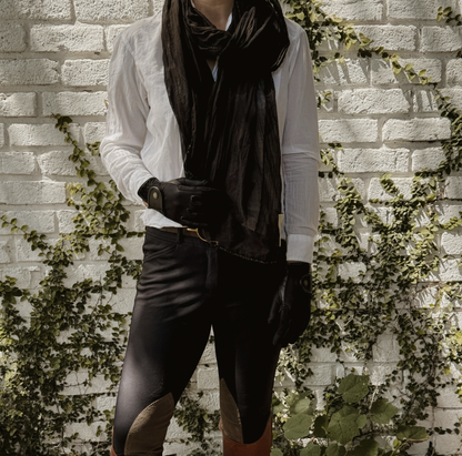Equestrian wearing a black voile scarf standing next to a white brick wall with green vines