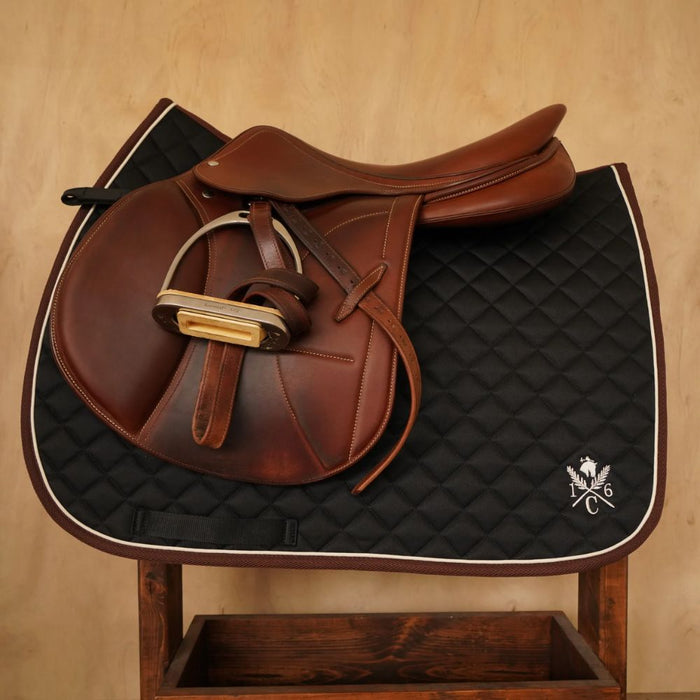 Black diamond‑quilted saddle pad with ivory piping and embroidered 16C crest on wooden stand