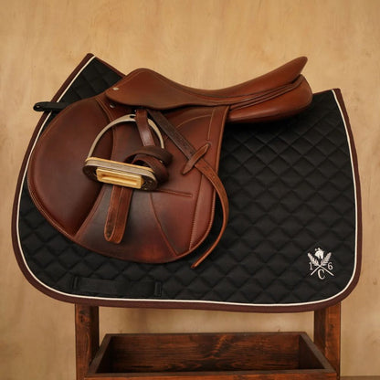 Black diamond‑quilted saddle pad with ivory piping and embroidered 16C crest on wooden stand