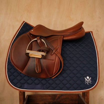 navy jumper saddle pad with cognac binding cream piping and english saddle on a wood stand