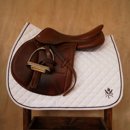 Brown English saddle on a white quilted jumper saddle pad with Hickory piping and 16C crest